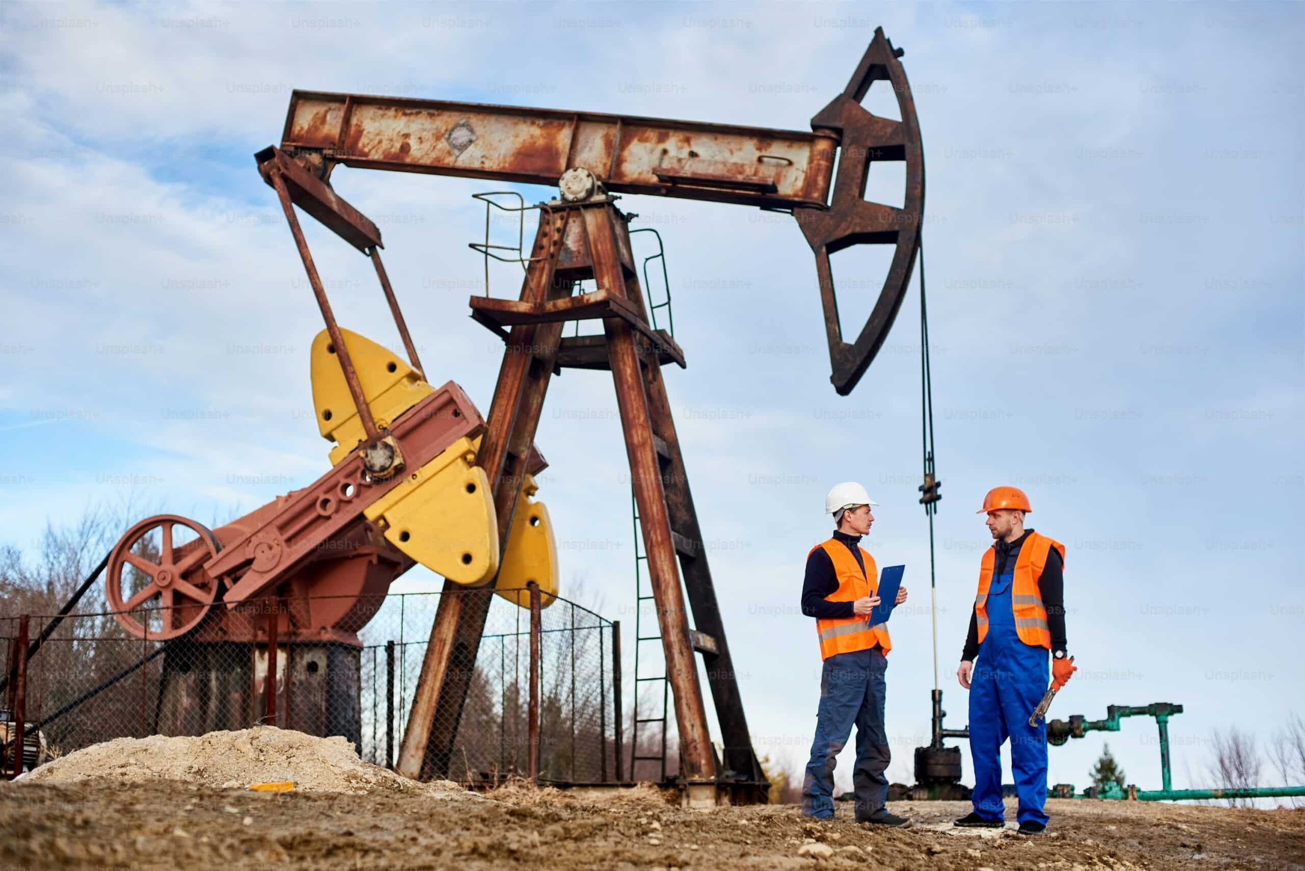 Two oil workers stand next to an oil jack on a well site to take readings.